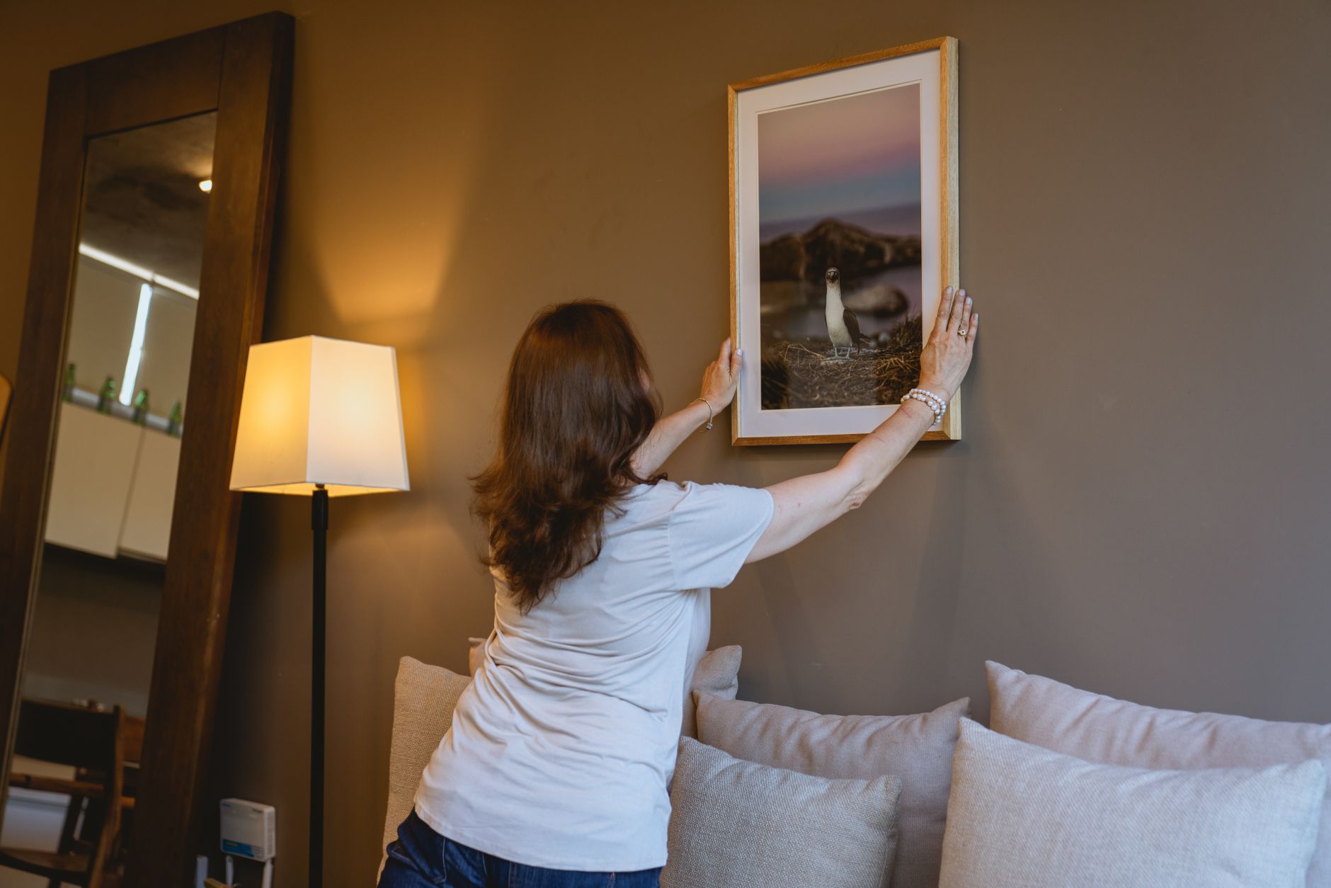 woman in white shirt hanging a frame on the wall